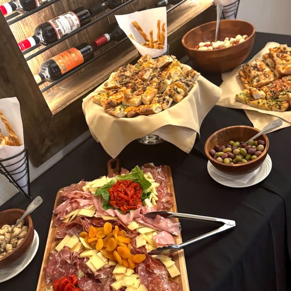 A buffet spread with Italian appetizers like focaccia, charcuterie, olives, and wine bottles.