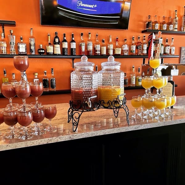 A bar with two drink dispensers, two champagne glass towers, and liquor bottles on shelves.