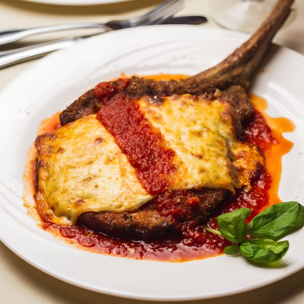 Veal Milanese with melted cheese and tomato sauce, garnished with fresh basil on a white plate.