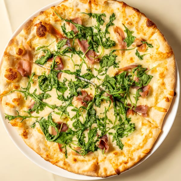 A whole Italian pizza with prosciutto, mozzarella, and fresh arugula on a white plate.