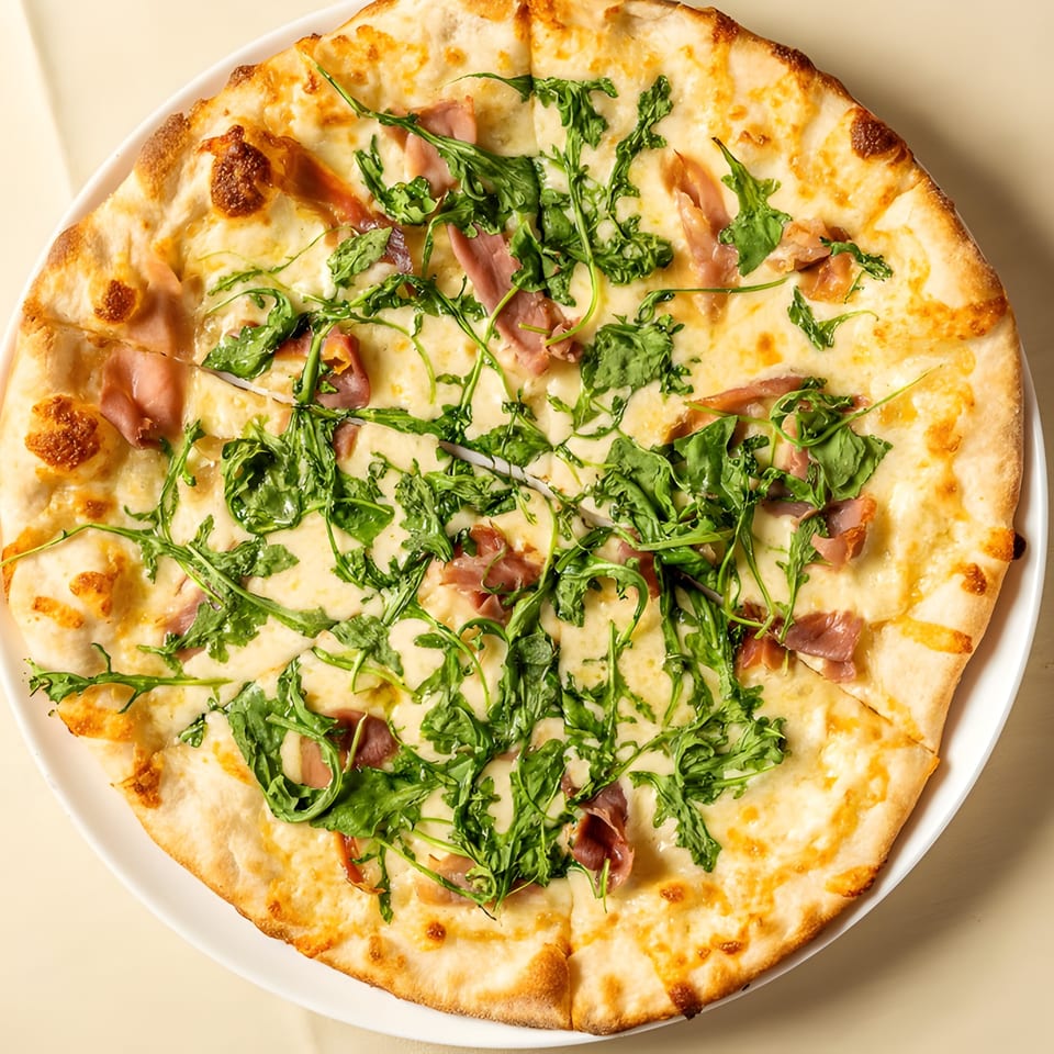 A whole Italian pizza with prosciutto, mozzarella, and fresh arugula on a white plate.